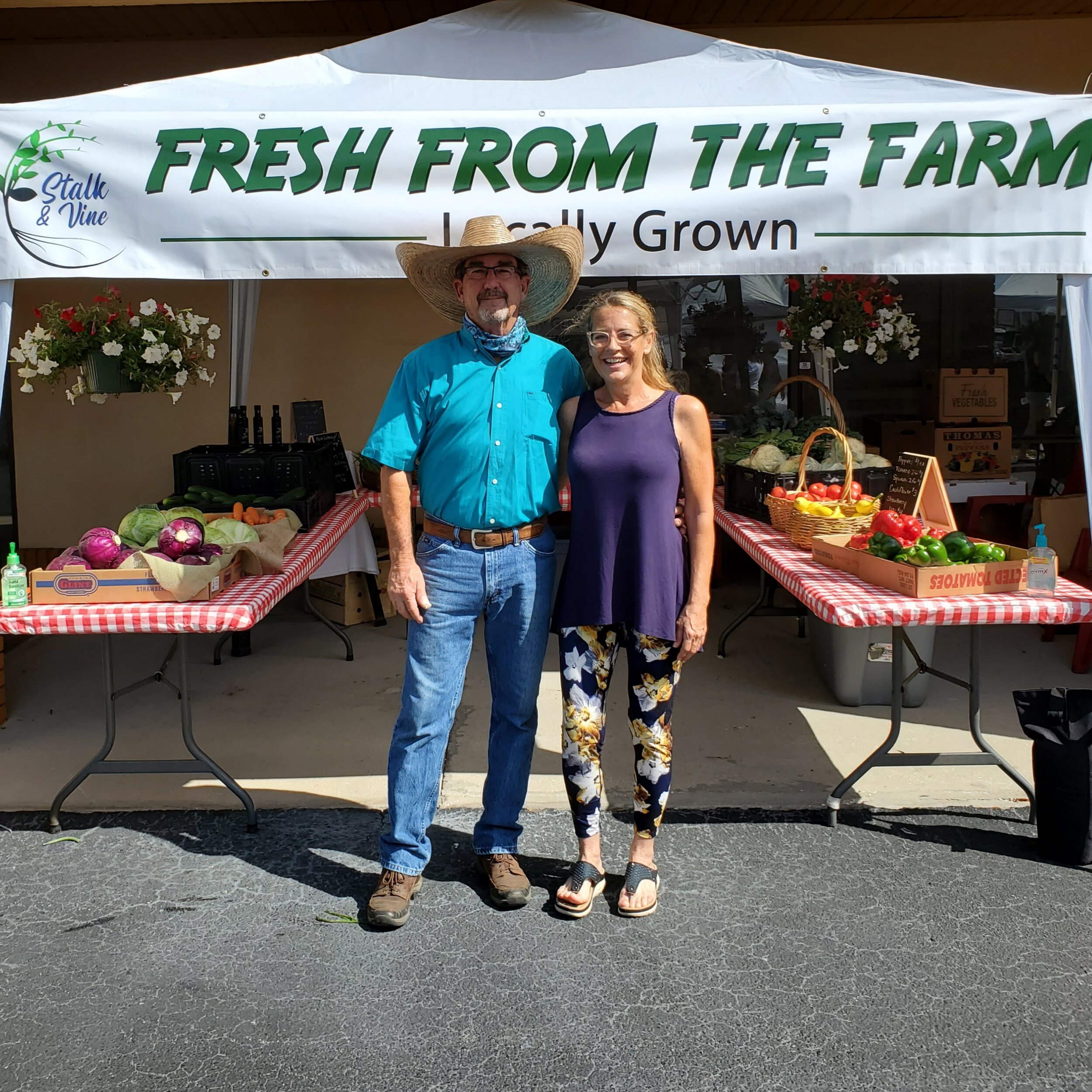 A farmer and a woman stand together at a local farmers market booth labeled 